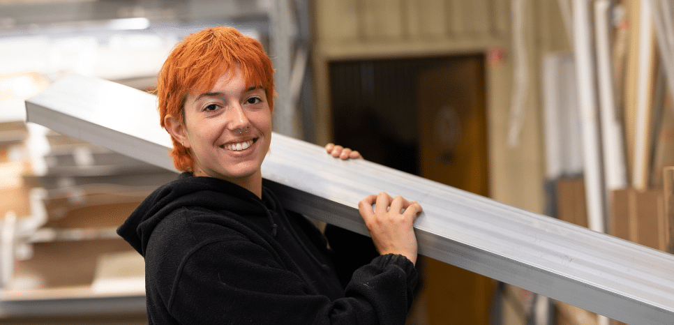 Personne portant un objet métallique sur l’épaule dans un atelier, symbolisant une entreprise de construction.
