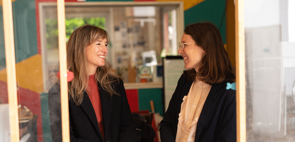 Deux femmes face à face, souriantes, dans un environnement professionnel.